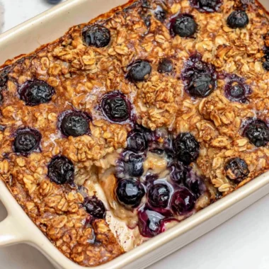 A warm dish of healthy blueberry baked oatmeal topped with fresh blueberries