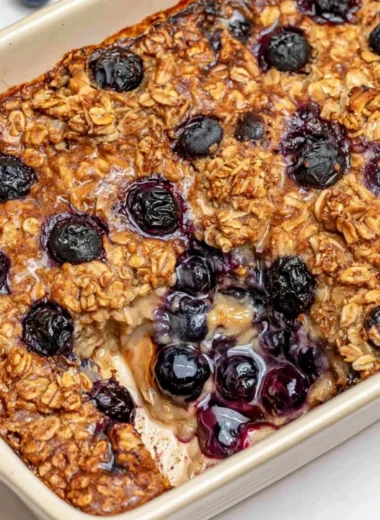 A warm dish of healthy blueberry baked oatmeal topped with fresh blueberries