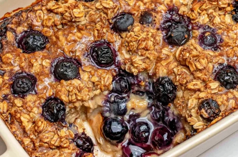 A warm dish of healthy blueberry baked oatmeal topped with fresh blueberries